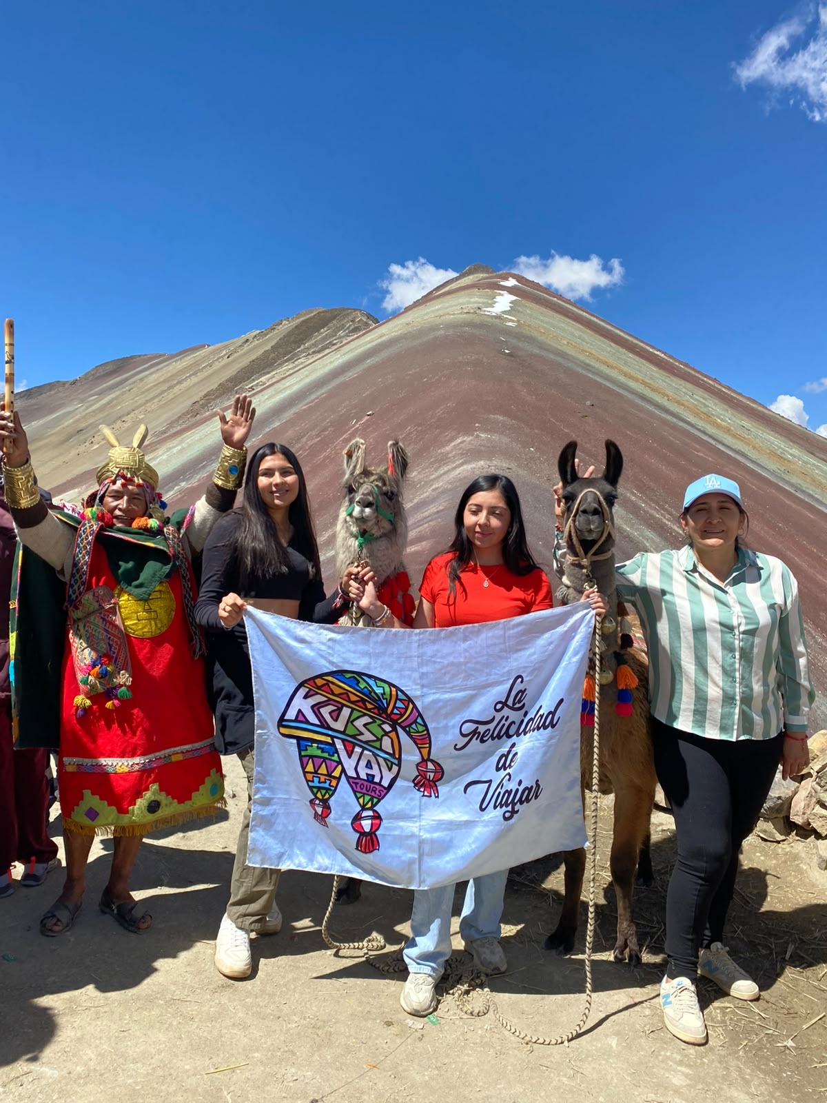 Viajeras de Kusiyay con llamas y la bandera de la marca en Vinicunca