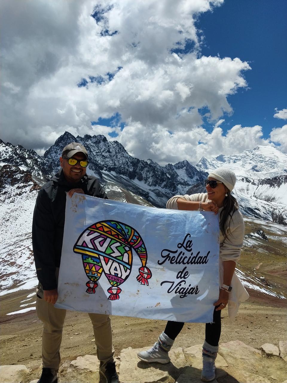 Pareja de Kusiyay sosteniendo la bandera ante el nevado Ausangate