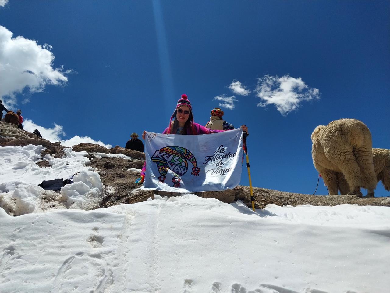 Viajera de Kusiyay mostrando la bandera entre nieve y alpacas