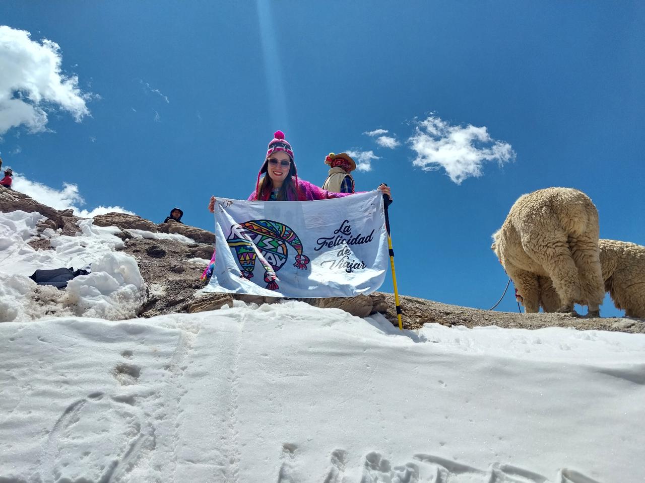Viajera sonriendo con la bandera de Kusiyay en la cordillera